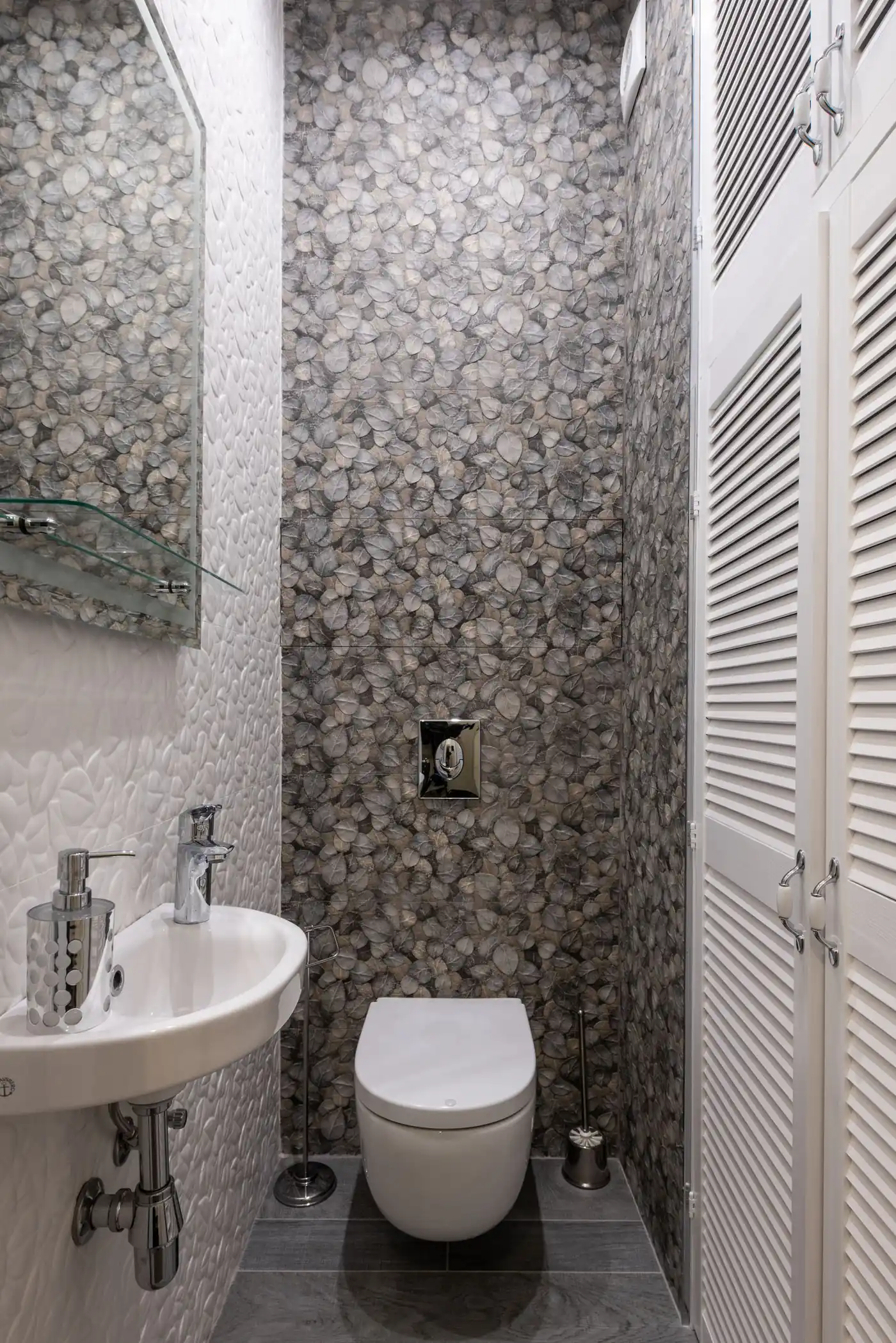 Compact bathroom with patterned stone-look tile, a small wall-mounted sink and a wall-hung toilet