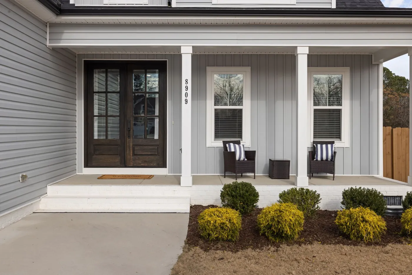 Gray suburban house with a covered front porch and neatly trimmed shrubs